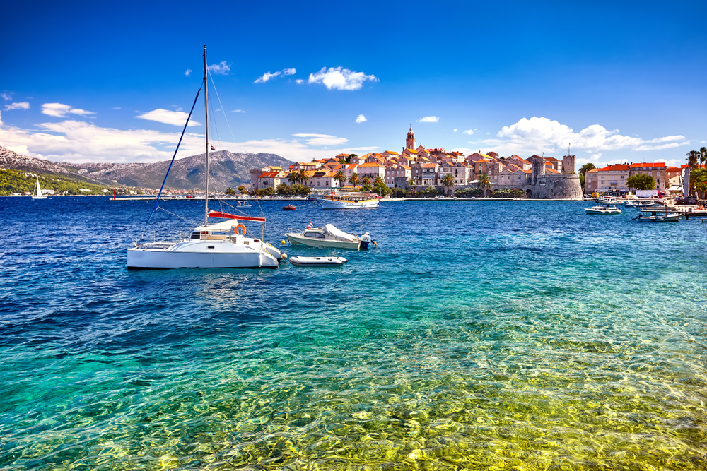 View from the sea at a sailing boat and a few vessels in front view, and the old town center in Korcula in the rear view, in Croatia.