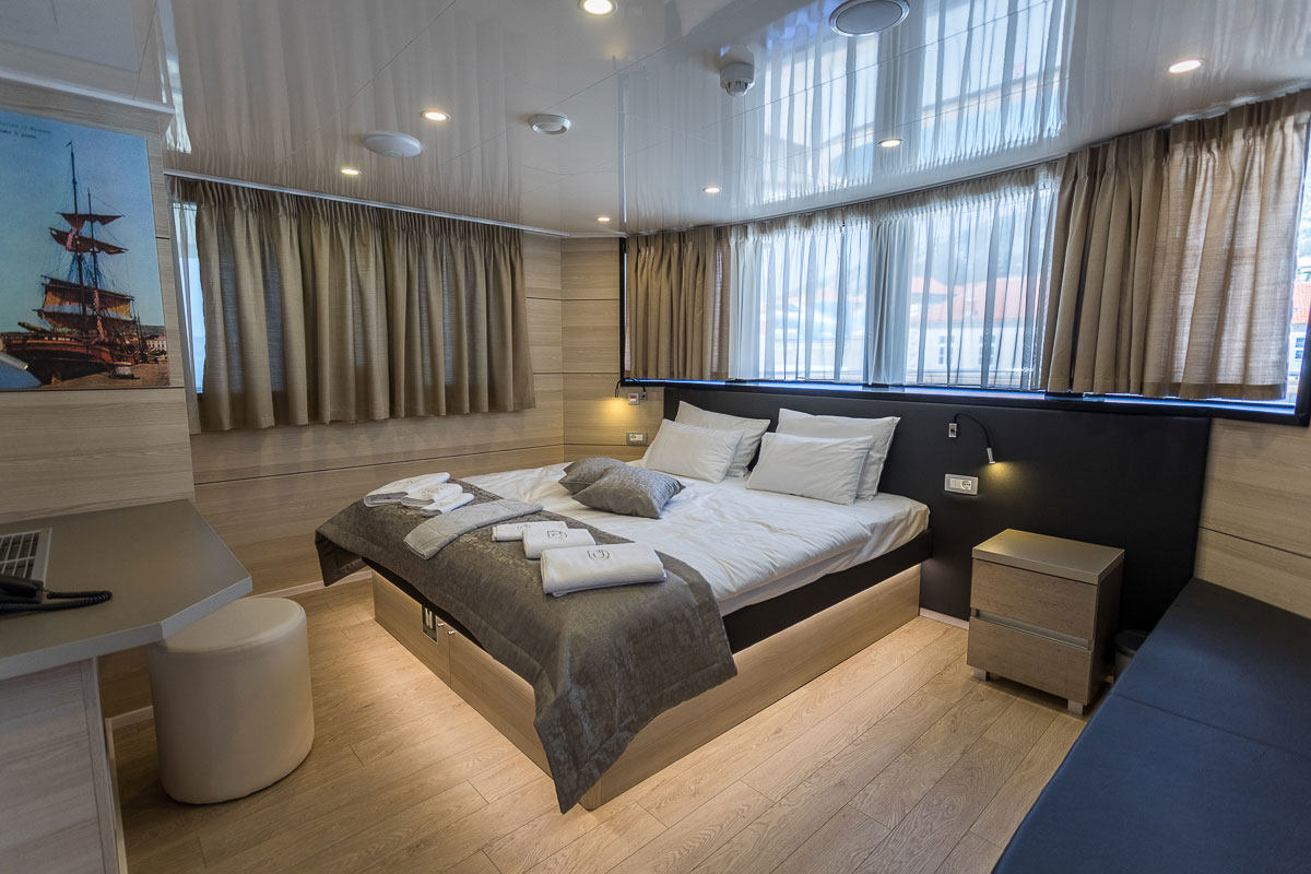 Desire Croatia Cruise ship cabin with a double bed, a small dressing table, big windows, and a small lounge area.