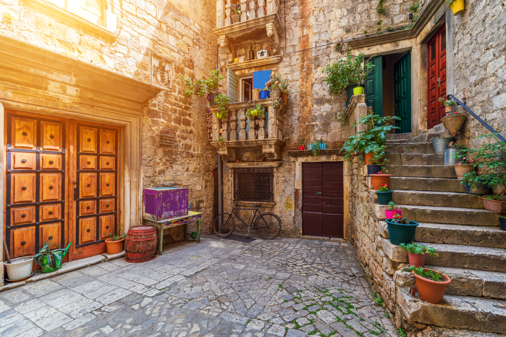 Narrow cobbled street with stone buildings in historic Trogir town in Croatia.