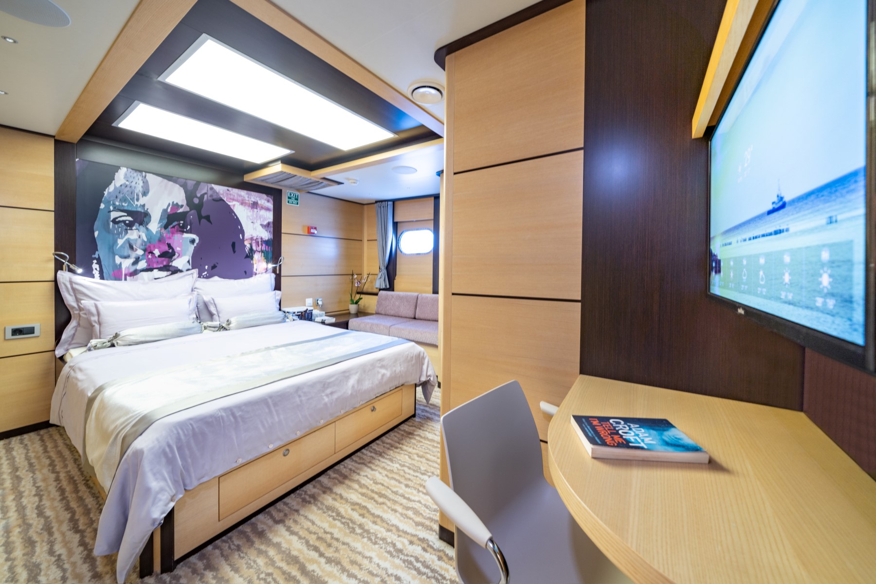 Navilux motor sailing yacht - cabin with a double bed, porthole, TV, and a dressing table.