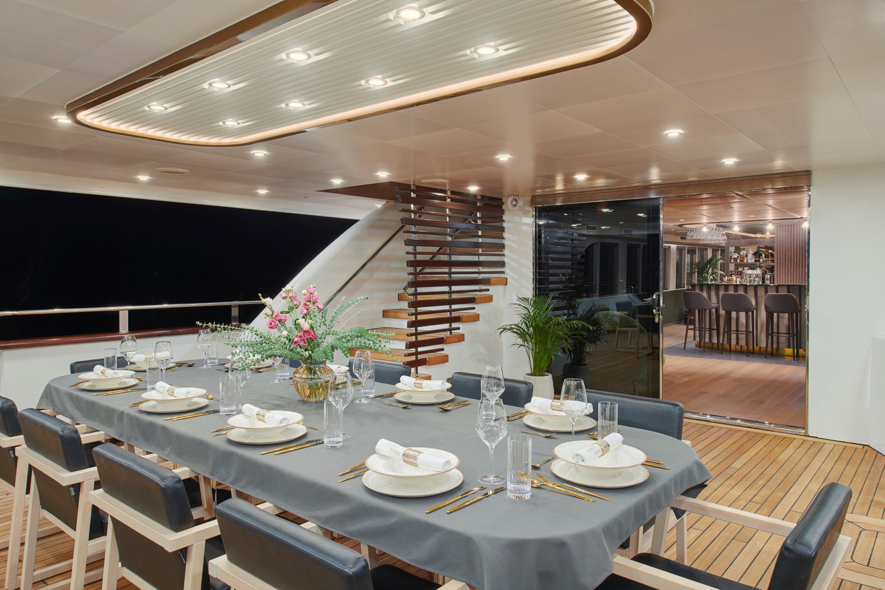 Anima Maris sailing yacht - stern lower deck outdoor covered dining table overlooking bar in the salon and stairs for the sun deck - night shot.
