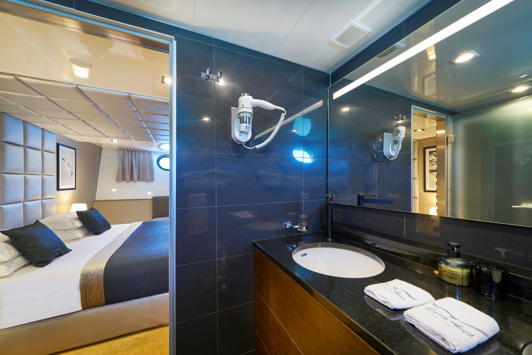 Rara Avis sailing yacht - black tiled bathroom and a cabin with a double bed and a porthole.
