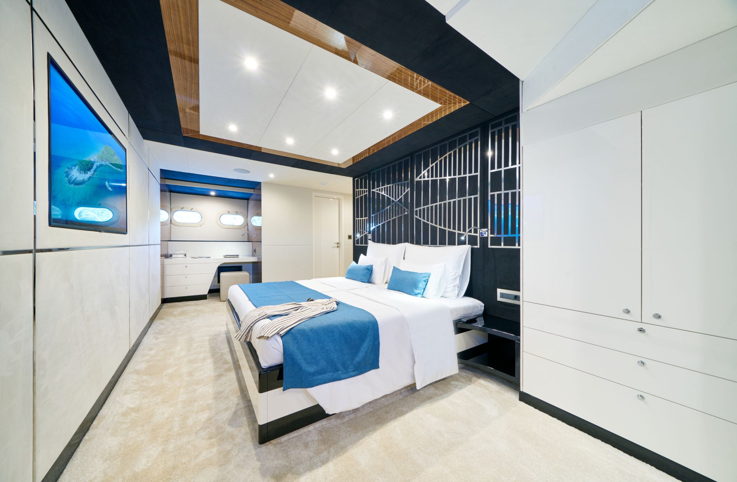 Acapella luxury charter yacht ensuite cabin with a double bed, TV, 2 portholes, and a dressing table.