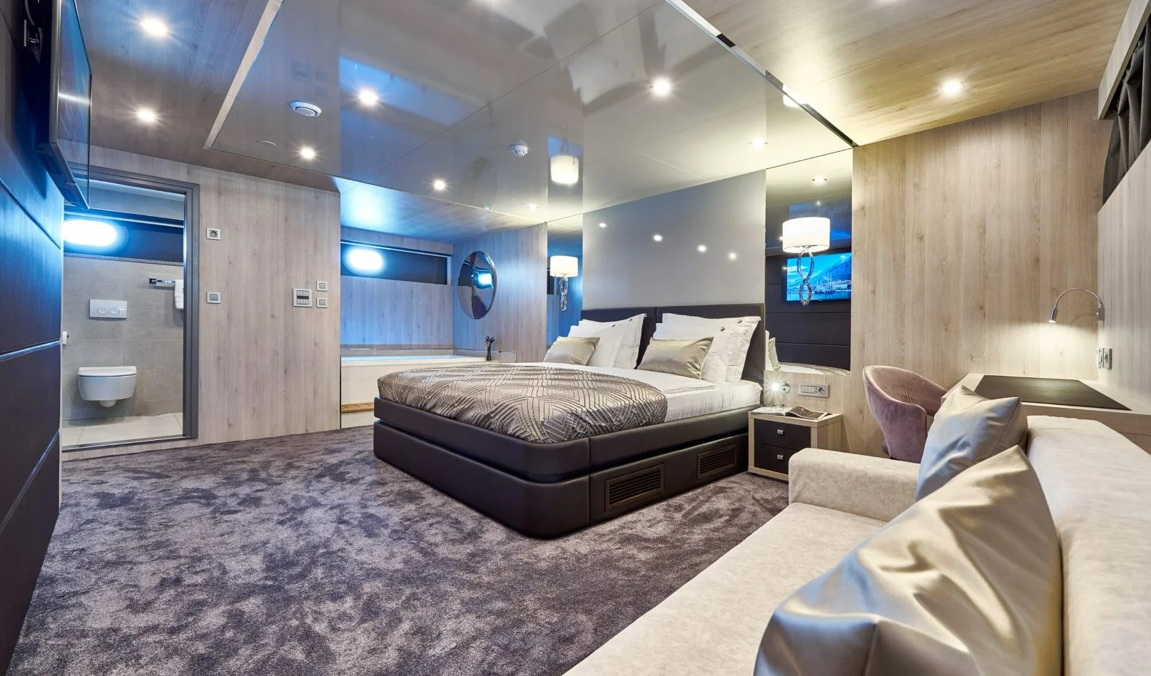 Dalmatino yacht master cabin with double-bed, a massage tub, sofa and an office table, TV and opened door of a bathroom