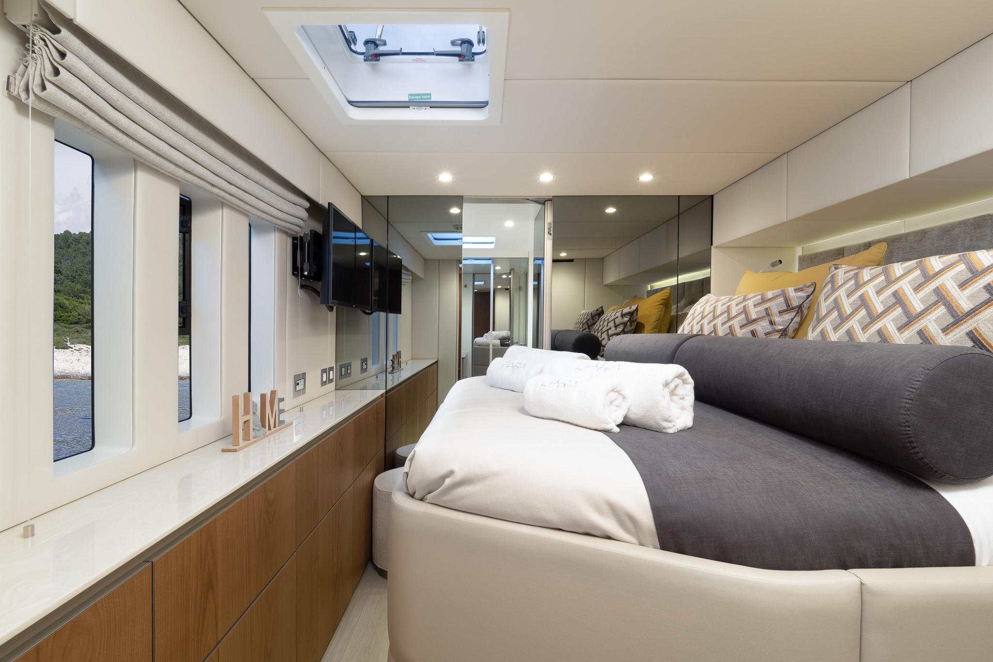 Sunreef 50 ZARA luxury catamaran ensuite cabin with a double bed and several big windows and a roof window with bathroom doors opened and a TV