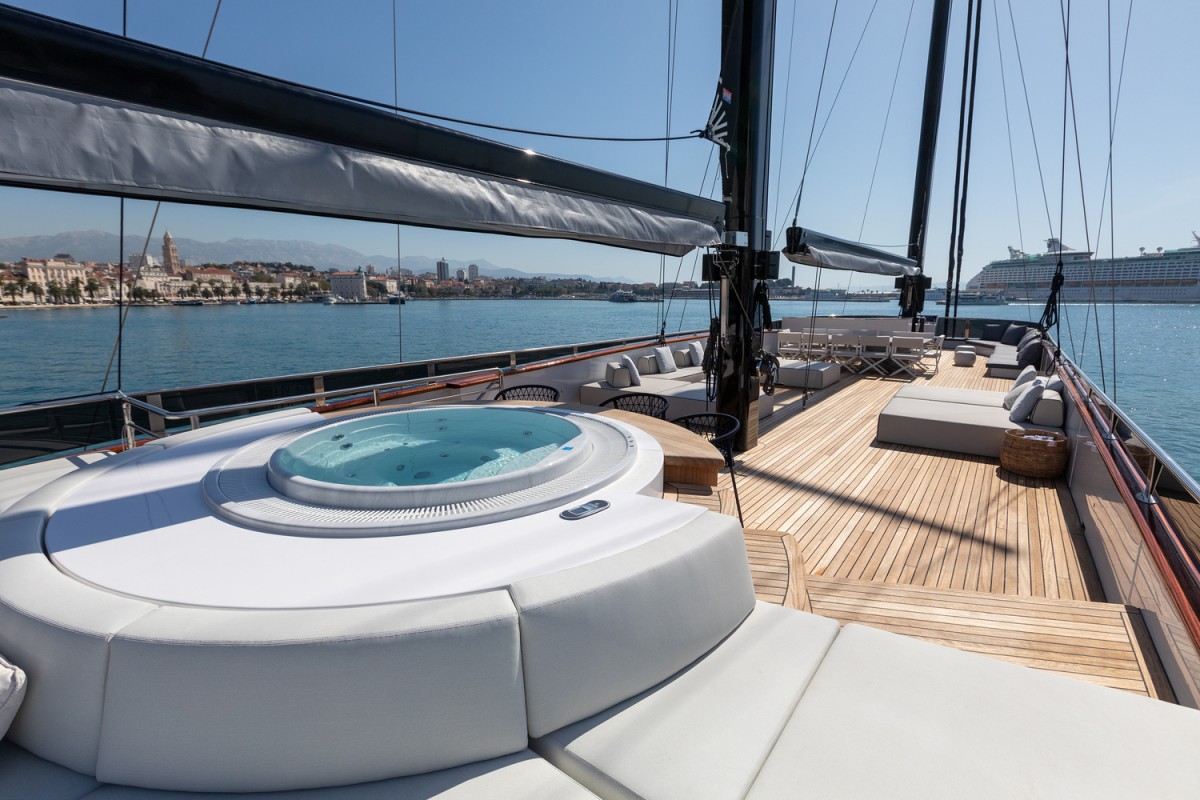 Sun deck with a jacuzzi, lounge area, sunbeds, and dining table on the Scorpios sailing yacht.